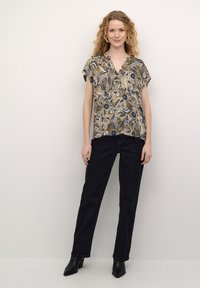 Blusa con motivo floreale in tonalità di beige e blu navy, maniche corte, scollatura a V; abbinata a jeans in denim scuro a gamba dritta e stivali neri con tacco.