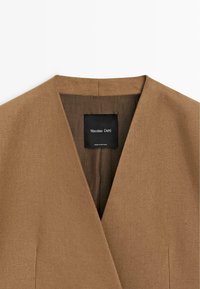 Bruine V-hals kleding met een zichtbaar zwart label waarop staat "Massimo Dutti, Made in Portugal" aan de binnenkant bij de kraag.