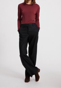 Bordeaux rood langemouwshirt gecombineerd met een hoog-wajige zwarte wijde broek met zijzakken en een gladde textuur. Bruine enkellaarsjes maken de look compleet.