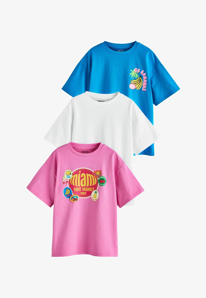 Trois t-shirts à manches courtes et col rond : un bleu avec un motif banane, un blanc uni et un rose avec des patchs colorés de marché aux fruits.