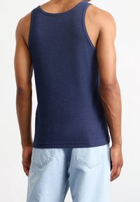 Navy ribbed tank top with wide shoulder straps, featuring a relaxed fit and a smooth texture, paired with light blue loose-fitting jeans.
