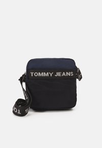 Granatowa torba na ramię z zamkiem błyskawicznym, panel z siatki oraz regulowanym paskiem z logo "TOMMY JEANS" w kontrastującym białym kolorze.
