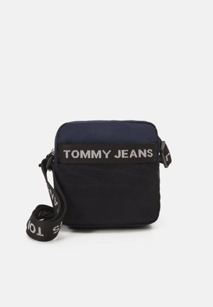 Granatowa torba na ramię z zamkiem błyskawicznym, panel z siatki oraz regulowanym paskiem z logo "TOMMY JEANS" w kontrastującym białym kolorze.