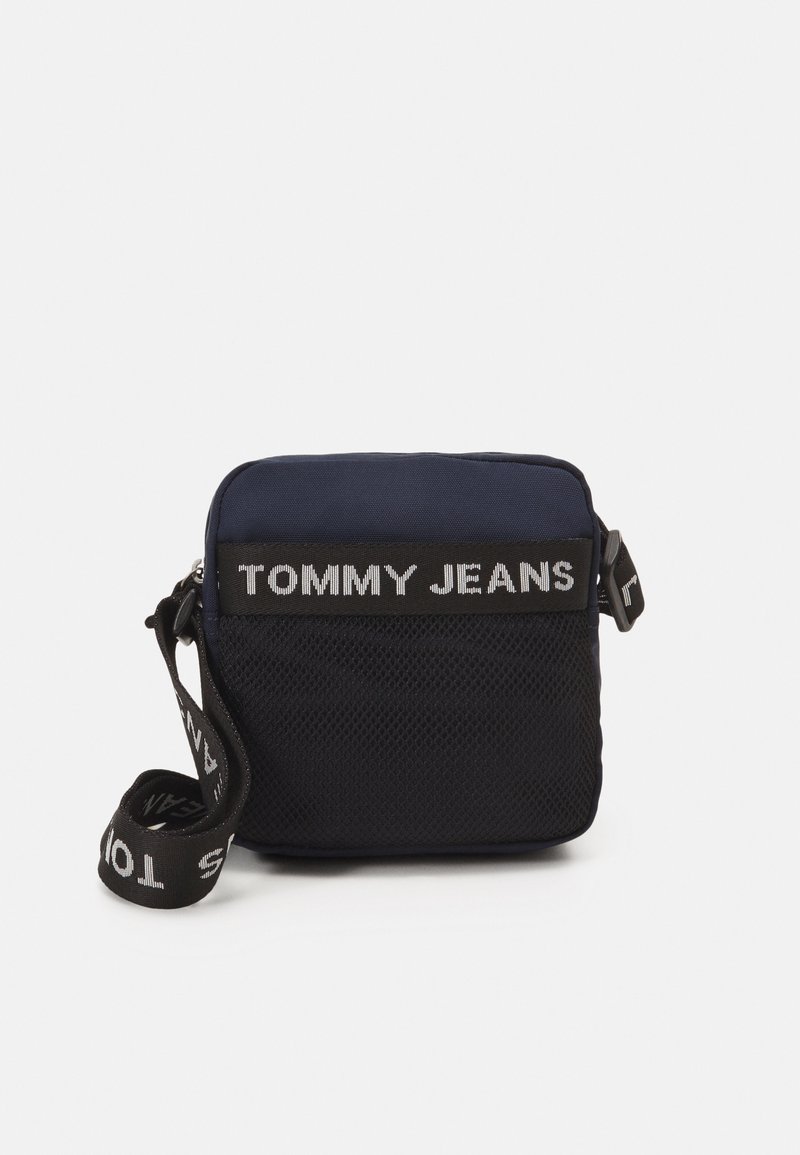 Granatowa torba na ramię z zamkiem błyskawicznym, panel z siatki oraz regulowanym paskiem z logo "TOMMY JEANS" w kontrastującym białym kolorze.