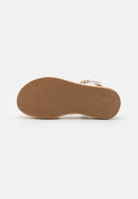 Brown rubber sole with textured pattern, combined with woven edge. Light tan color, flat design, smooth surface, and no visible hardware.