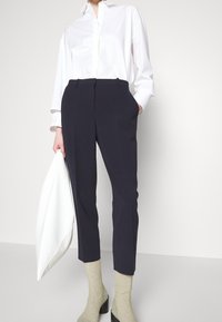 Pantalones entallados de color azul marino con una textura suave, que cuentan con bolsillos delanteros y un corte ajustado. Combinados con una camisa blanca de botones y calcetines color crema.