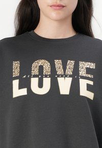 Felpa grigia scura con grande scritta "LOVE". Le lettere sono una combinazione di stampa leopardata e crema uniforme. Il testo è posizionato centralmente con scollo rotondo.