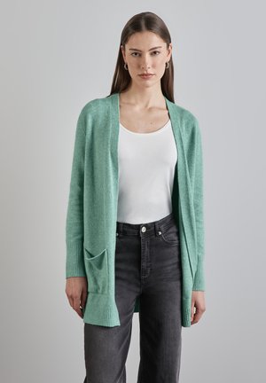 Cardigan vert menthe clair en tricot doux, avec une ouverture à l'avant, des poignets côtelés et une poche avant unique. Assorti à un haut blanc et un jean noir.