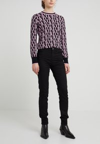 Svart stickad tröja med rosa logomönster, rund halsringning och ribbade ärmslut, tillsammans med svarta slim-fit jeans och svarta klackstövletter.