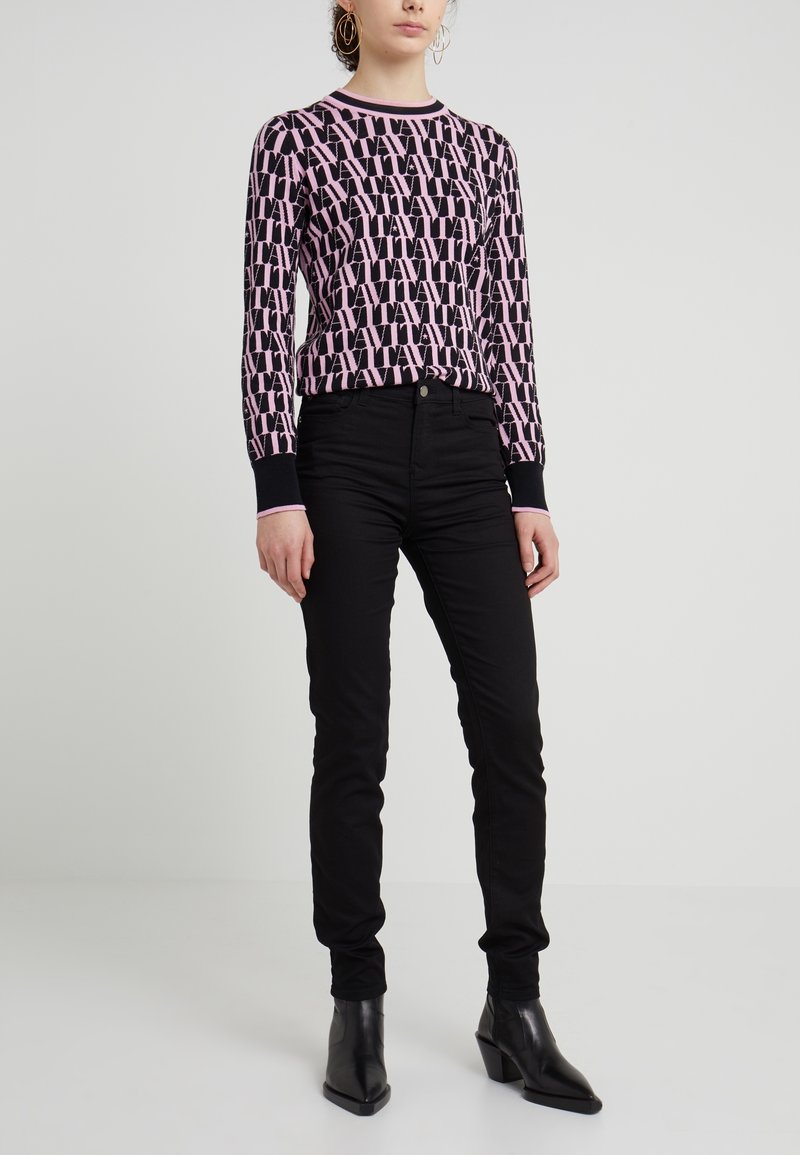 Svart stickad tröja med rosa logomönster, rund halsringning och ribbade ärmslut, tillsammans med svarta slim-fit jeans och svarta klackstövletter.