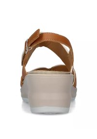 Sandali in pelle marrone con schiena aperta, cinturino regolabile e suola spessa di colore chiaro con un leggero motivo testurizzato.