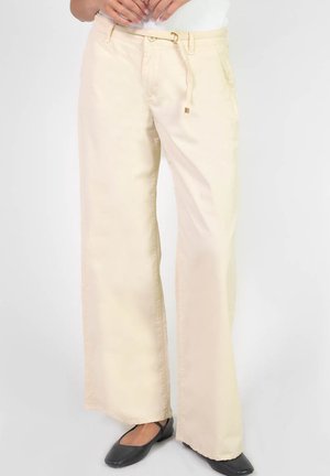 Pantalons larges beiges en tissu lisse, avec une taille élastique à cordon et des poches, portés avec des ballerines noires.