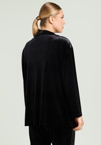 Black velvet long-sleeve shirt with a relaxed fit, flat collar, and seamless shoulders. Smooth texture and a slightly longer back hem.