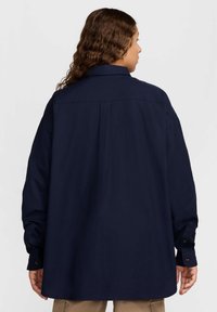 Camisa azul marinho de manga longa com colarinho clássico, punhos com botão e um corte descontraído, apresentando um yoke nas costas e uma textura subtil.
