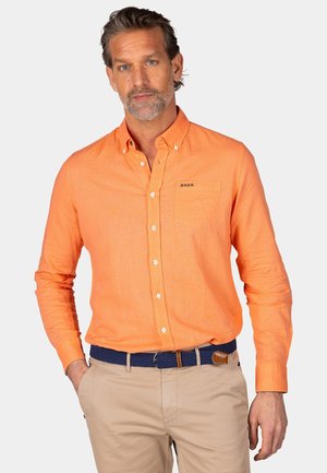 Oranje overhemd met knopen en een zak, voorzien van een subtiele logo. De stof lijkt licht en textuur te hebben. Gecombineerd met lichtbeige trousers.