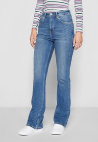 Jeans de mezclilla azul acampanados con una cintura alta, que presentan un diseño clásico de cinco bolsillos y sutiles detalles de costura. Textura suave.