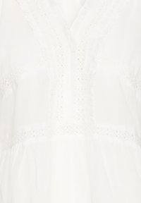 Tissu blanc avec inserts en dentelle et bordure à volants formant des motifs décoratifs verticaux et horizontaux.