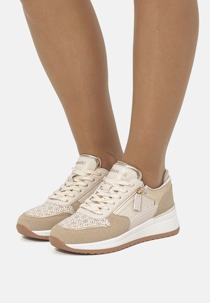 Zapatillas deportivas beige con una parte superior de cuero liso y diseño perforado. Cuenta con una suela acolchada y una suela exterior de goma en contraste.
