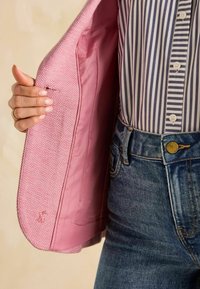 Rosa kalastriibuline jakk, millel on sile sisemine vooder, koos tumeda navü ja valge triibulise särgi ning teksapükstega.