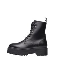 Bottes de combat en cuir noir à la cheville haute, à lacets, avec une semelle plateforme épaisse et une bande de roulement en caoutchouc texturé. Elles comportent une languette à l'arrière.