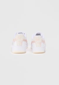 White sneakers with pink accents, featuring a smooth leather upper, padded collar, and textured rubber outsole. Subtle logo design on heel.