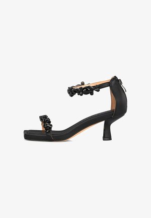 Schwarze High-Heelsandalen mit offenen Zehen, strukturierte Lederoberfläche, dekorative schwarze Schmuckakzente am Knöchelriemen und einem eleganten Blockabsatz.