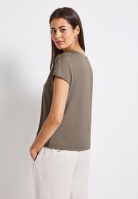 Khaki t-shirt z krótkim rękawem, okrągłym dekoltem, gładką tkaniną i luźnym krojem. W komplecie z lekkimi lnianymi spodniami z bocznymi kieszeniami.