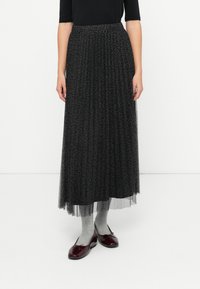 Plisseret svart tyllskjørt med et subtilt leopardmønster, med elastisk midje, iført grå sokker og burgunder ballerinaer.