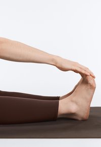 Jambes étendues sur un tapis de yoga, mains tendues vers l'avant pour saisir les orteils lors d'une flexion avant assise.