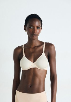 Light beige bra made of smooth fabric with molded cups, adjustable straps, and minimal stitching. Features a subtle, structured design.