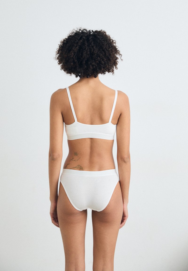 Set di bralette in cotone bianco e slip a gamba media. Design semplice con spalline sottili, texture liscia e cintura elastica. Nessun motivo né accento.