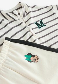 Pasiasty rozpinany top w kolorze off-white i szarym z haftem litery 'M' w kolorze zielonym; zestawiony z szortami w kolorze off-white z czarnym wykończeniem i nadrukiem Myszki Minnie.