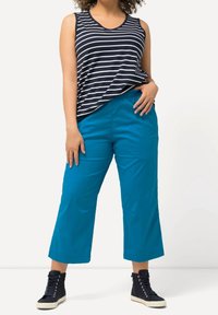 Marineblauw en witte gestreepte mouwloze top gecombineerd met felblauwe, loszittende, korte broek. Zwarte hoge sneakers. Eenvoudige, casual outfit.