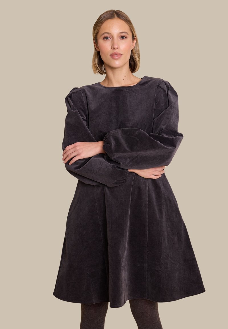 Mørkegrå kordfløjlskjole med lange puffærmer og rund halsudskæring, der har en svajende nederdel og en blød tekstur.