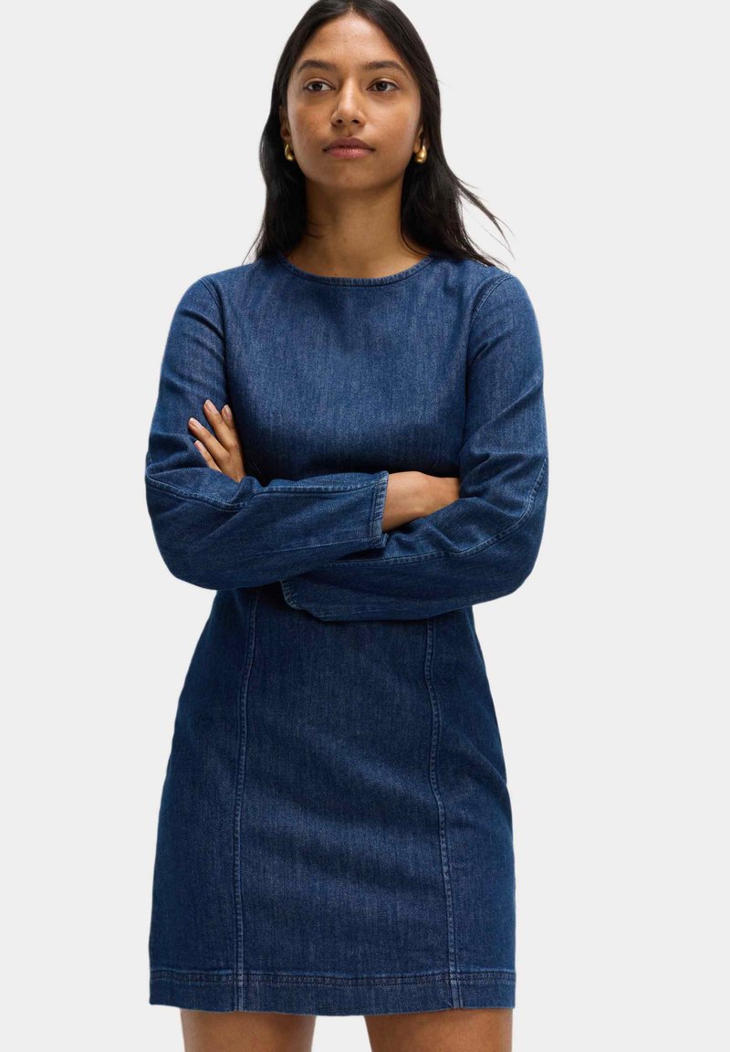 Denimklänning med rak silhuett, långa ärmar, rund halsringning, mörkblå färg och synliga sömnadsdetaljer.