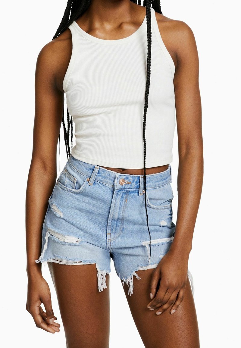 Valkoinen ribattua kangasta oleva tankkitoppi ja vaaleansiniset kulutetut farkkushortsit, joissa on frayed-reunat, nappikiinnitys ja useita repeämiä.