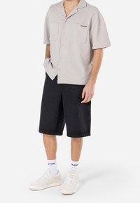 Lyhythihainen, vaalea harmaa nappipaita, jossa on tekstiilityyppinen kangas, kaksi etupainiketta, yhdistettynä mustiin farkkushortseihin ja valkoisiin lenkkareihin.