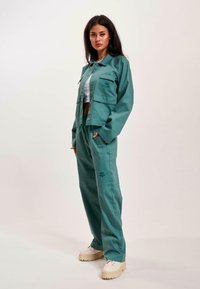 Türkise, cropped Jacke und passende Hosen mit lockerer Passform. Mit Fronttaschen und Logodetail. Getragen mit hellen, klobigen Schuhen.