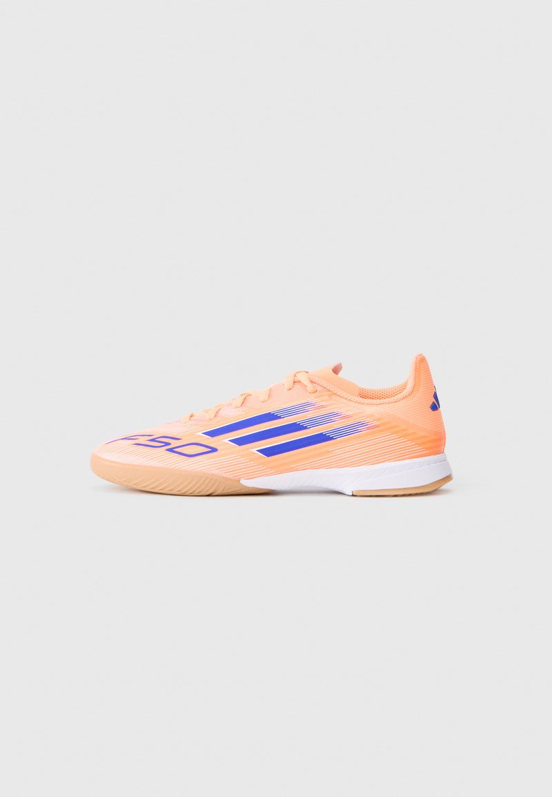 Scarpa da calcetto indoor a profilo basso color pesca con strisce blu, testo "GSO", suola bianca e chiusura con lacci, mostrata di lato su uno sfondo neutro.