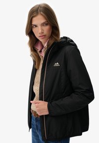 Zwarte jas met rits en capuchon en elastische manchetten, met een gestructureerde afwerking, roze accenten en een driehoekig logo op de borst.