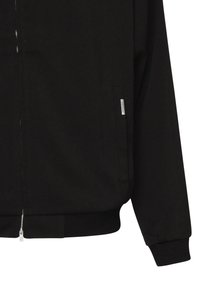 Chaqueta negra con cremallera y puños y dobladillo acanalados, con un bolsillo lateral que presenta una pequeña etiqueta de la marca "Represent".