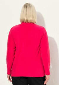 Fleece bunda v jasně růžové barvě, s dlouhými rukávy, těsně střihová s detaily švů, bez viditelného hardwaru nebo vzorů. Zobrazeno ze zadní strany.