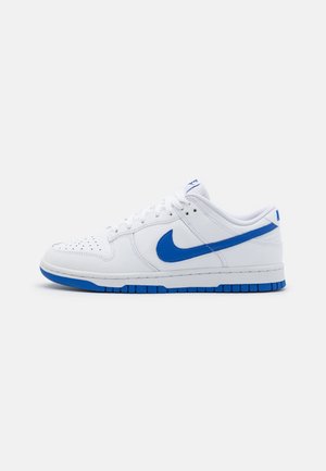 Zapatillas de cuero blanco con un swoosh azul de Nike, que presentan un diseño perforado en la puntera, cordones blancos y una suela de goma azul.