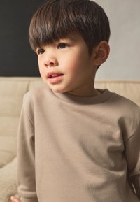 Bluza bej cu mâneci lungi, din țesătură moale, cu guler rotund, caracterizată printr-o croială lejeră și textură fină.