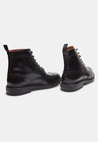 Botines de cuero negro con detalles de brogue, cierre de cordones y tira para el talón. Textura suave y punta redonda con tacón apilado.