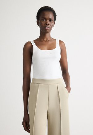 Witte geribde tanktop met een vierkante halslijn, gedragen met hooggesneden beige geplooide broek. Eenvoudig ontwerp, zonder patronen of accenten.