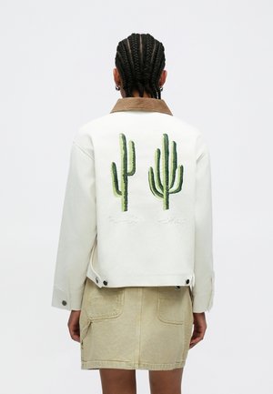 Balta džinsa jaka ar brūnu apkakli, uz muguras divi zaļi kaktusa izšuvumi un zem tiem vārdi "Paradise Utopias".