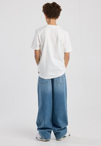White cotton t-shirt and blue wide-leg jeans. The jeans have a faded look with back pockets, finished with white sneaker accents.