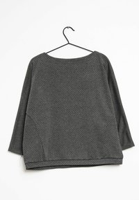 Camiseta de manga larga en gris oscuro con un patrón de diamantes, escote redondo y corte holgado. El material parece texturizado y suave. Se cuelga de un gancho negro.