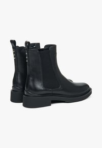 Černé kožené kotníkové boty s elastickými bočními panely, hladkým povrchem, kulatou špičkou a masivním podpatkem. Obsahují stříbrné akcenty na zadní straně.